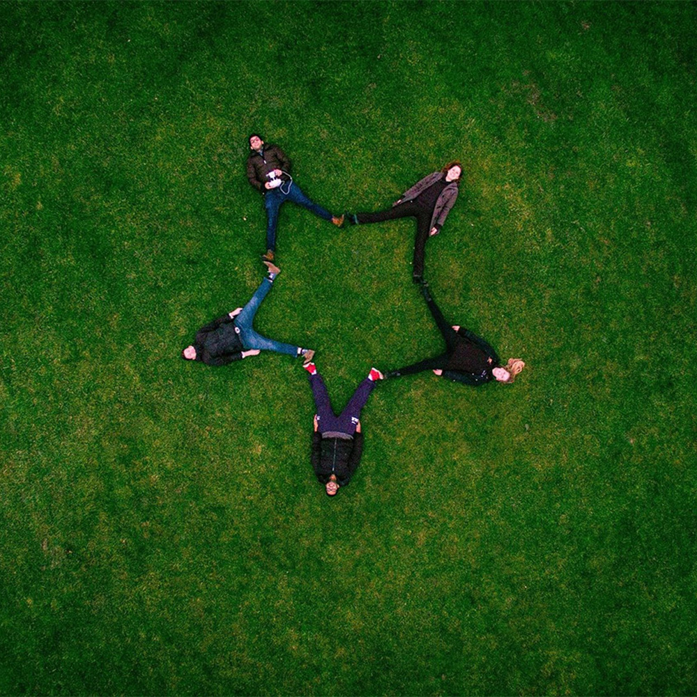 Vue aérienne de cinq personnes allongées sur l'herbe en formant une étoile avec leurs corps pour représenter l'étoile du logo d'Alyconis